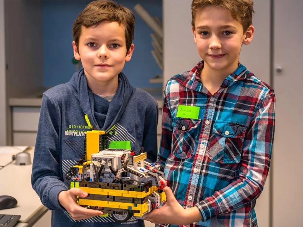 Zwei Jungen halten ein selbst gebautes Fahrzeug aus Lego in die Kamera.